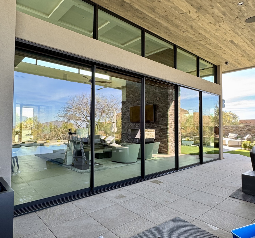 A large patio enclosed by glass walls, showcasing a swimming pool that enhances the outdoor ambiance A patio featuring sliding glass doors that open to a swimming pool, surrounded by greenery and outdoor furniture